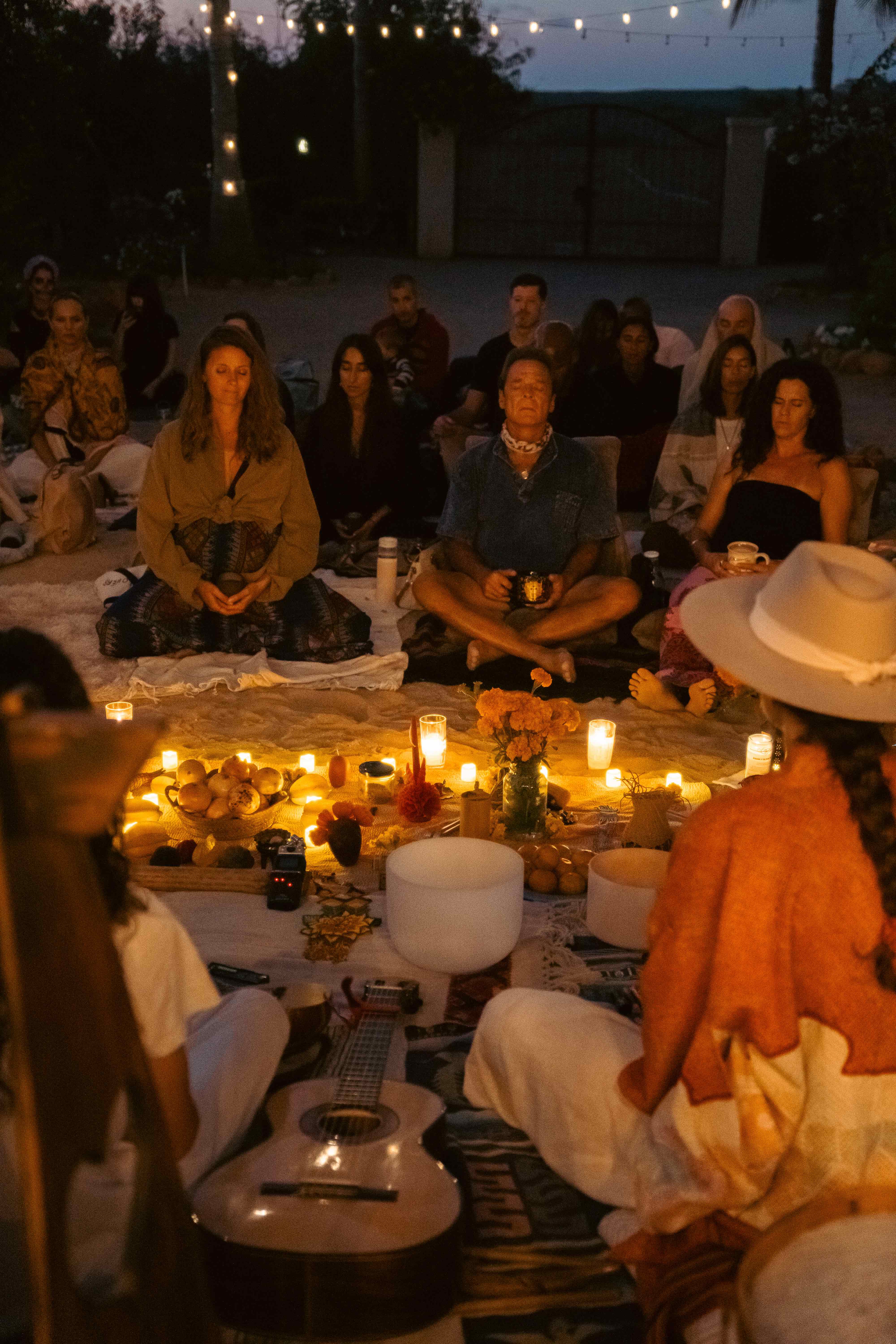 Community circle ceremony at dusk with candles, flowers, and sacred altar