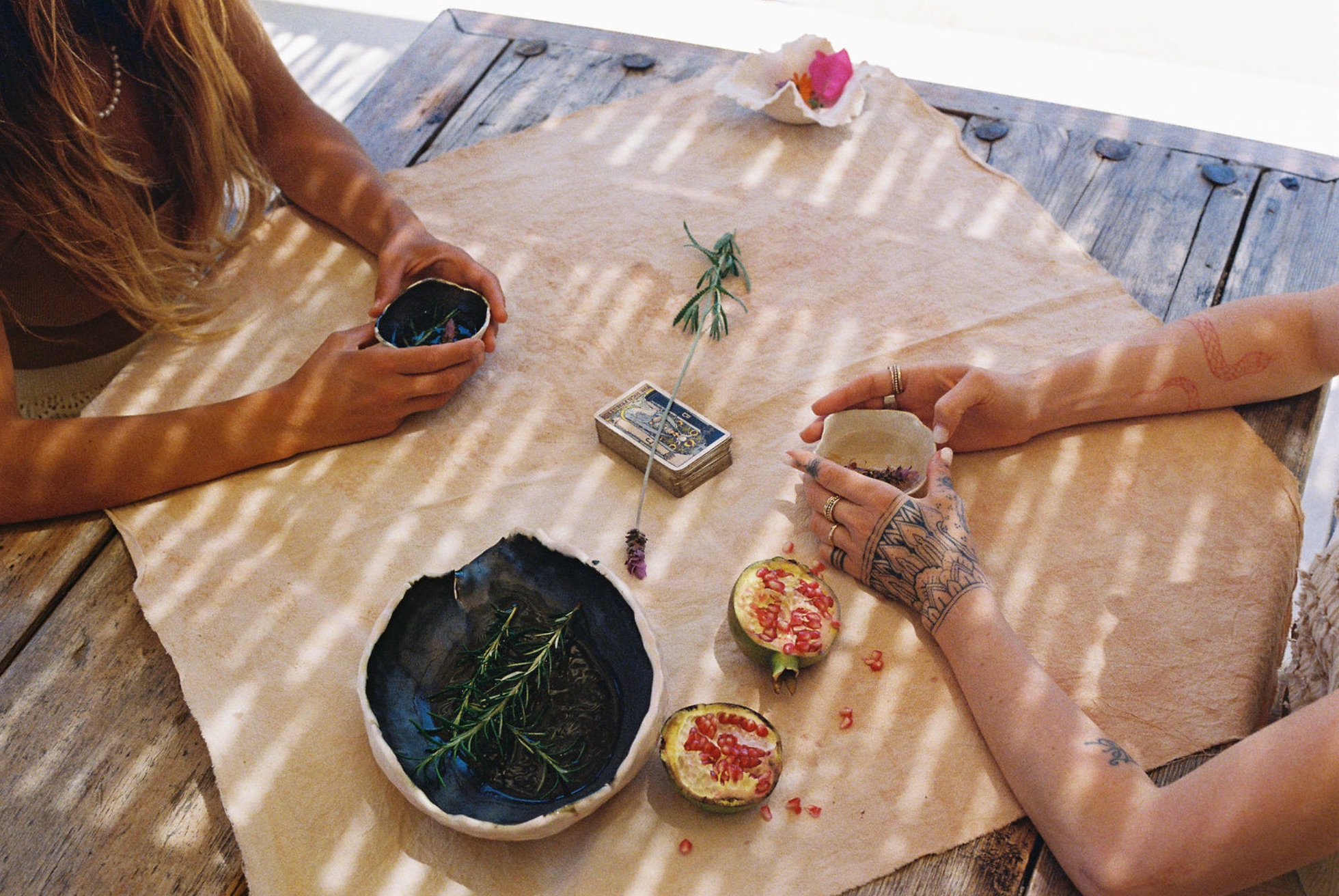Hands sharing ritual with tarot cards and botanicals on wooden deck
